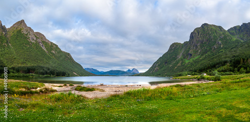 View from grassland to beach at lake Skarsvatnet among high mountains in evening in Norway island Amnoya.