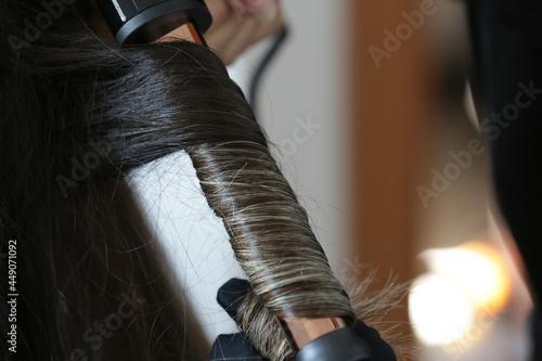 Fixing a woman's beautiful, blonde hair with a black curling iron.