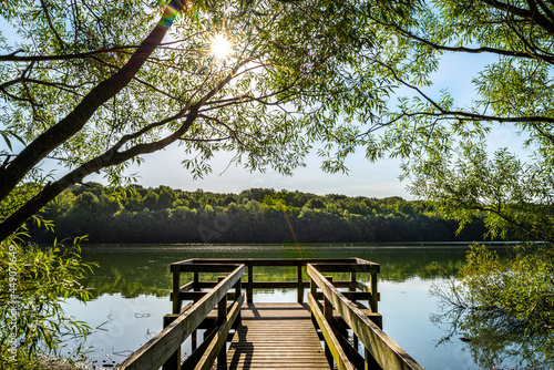 Konstfotografi Ruislip Lido wooden viewing platform over the water with Ruislip woods in the distance on a sunny day with sunburst