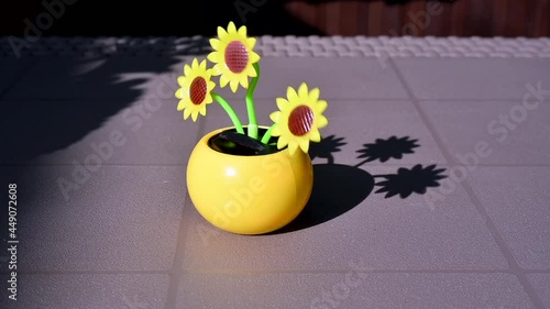 View on a solar powered plastic artificial sunflower moving by the sunlight representing renewable energy source on a table in the garden.