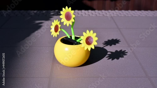 View on a solar powered plastic artificial sunflower moving by the sunlight representing renewable energy source on a table in the garden.