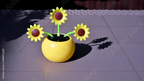 View on a solar powered plastic artificial sunflower moving by the sunlight representing renewable energy source on a table in the garden.