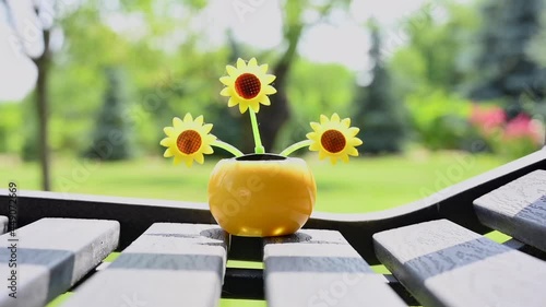 View on a solar powered plastic artificial sunflower moving by the sunlight representing renewable energy source on a bench in the garden.