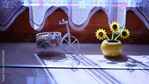 View on a solar powered plastic artificial sunflower moving by the sunlight representing renewable energy source in the window.
