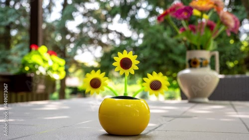 Time-lapse view on a solar powered plastic artificial sunflower moving by the sunlight representing renewable energy source on a table in the garden.