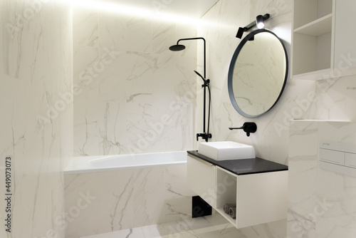 Modern spacious bathroom with marble tiles with a crisp white toilet, bathtub and sink. Side view. High-tech style.