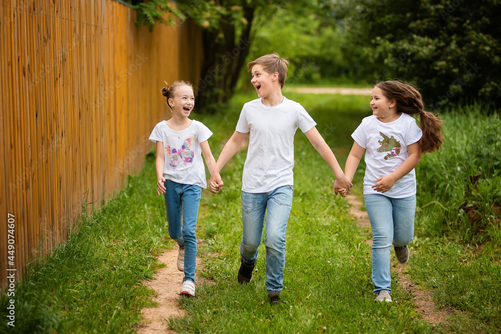 Cute little kids are running together on the road. Two sisters and a brother are holding hands, they are having fun, they are happy. The concept of childhood and friendship.