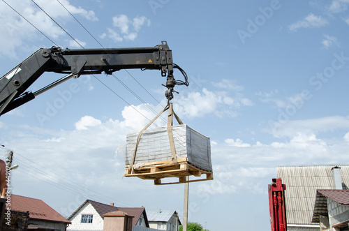 A man of a European race helps with loading tiles to the ground from a car. Delivery and unloading of building materials to the house. Truck crane unloaded street tiles.