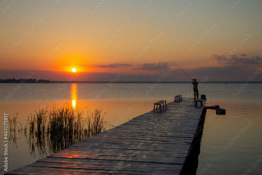 Morning fishing. A spinning fisherman is fishing in the lake. Rising Sun.