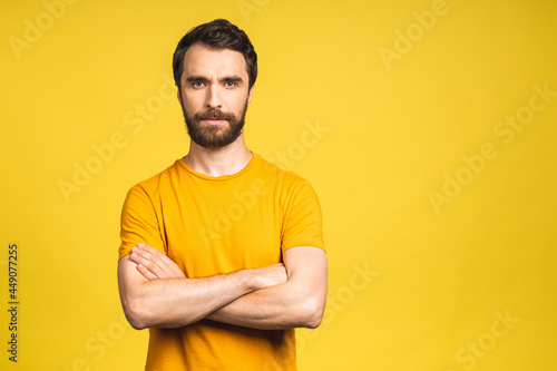 Portrait of serious fashionable handsome man in casual holding crossing hands and looking at camera isolated over yellow background.