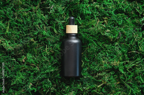 Black essential oil dropper bottle mockup on green moss background. Luxury cosmetic packaging template design. Flat lay, top view.