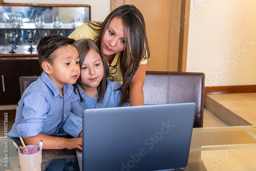 A mother with her male child and female daughter look at the computer in the dining room doing homework online