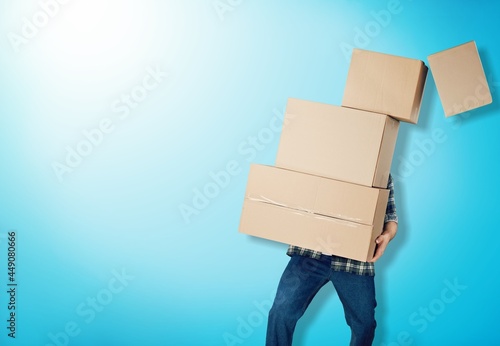Delivery man carrying stacked boxes in front of face against background