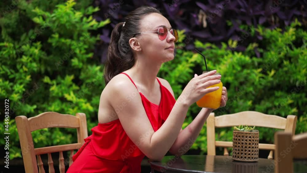 Confident beautiful female tourist drinking refreshing vitamin fruit cocktail sitting in outdoors cafe on Mediterranean resort. Slim gorgeous lady in red dress resting on sunny summer day outdoors Confident beautiful female tourist drinking refreshing vitamin fruit cocktail sitting in outdoors cafe on Mediterranean resort. Slim gorgeous lady in red dress resting on sunny summer day outdoors