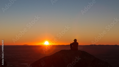 Pessoa curtindo o pôr do Sol no alto de uma montanha.