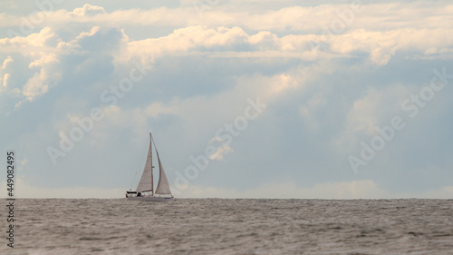 Veleiro navegando em um mar calmo com nuvens de tempestade ao fundo.