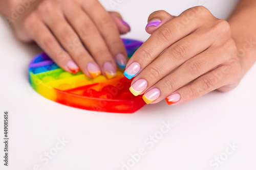 Beautiful female hands with colourful manicure nails holding toy, pop it