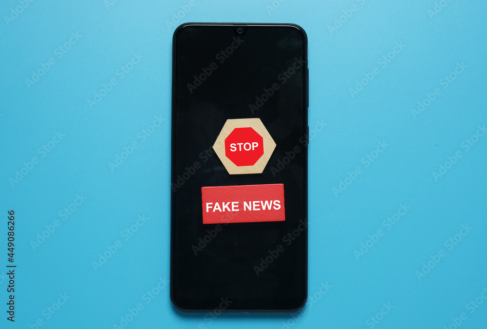A picture of stop sign on hexagon wood cut and fake news at red wood on smartphone. Fake new caused the hoax A picture of stop sign on hexagon wood cut and fake news at red wood on smartphone. Fake new caused the hoax