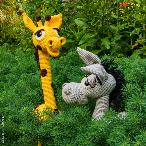 Handmade amigurumi dolls, a yellow giraffe and a gray donkey among the greenery of the garden.