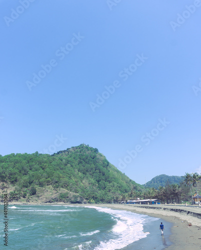 A person walking on the shore of Karang Bolong beach with a beautiful view of the ocean waves and hills. Summer theme. Travel and vacation