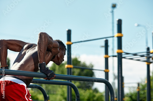 Black young man exercising on the uneven bars in the park, crossfit concept, african american man doing exercises on the uneven bars in the street, on the sports ground