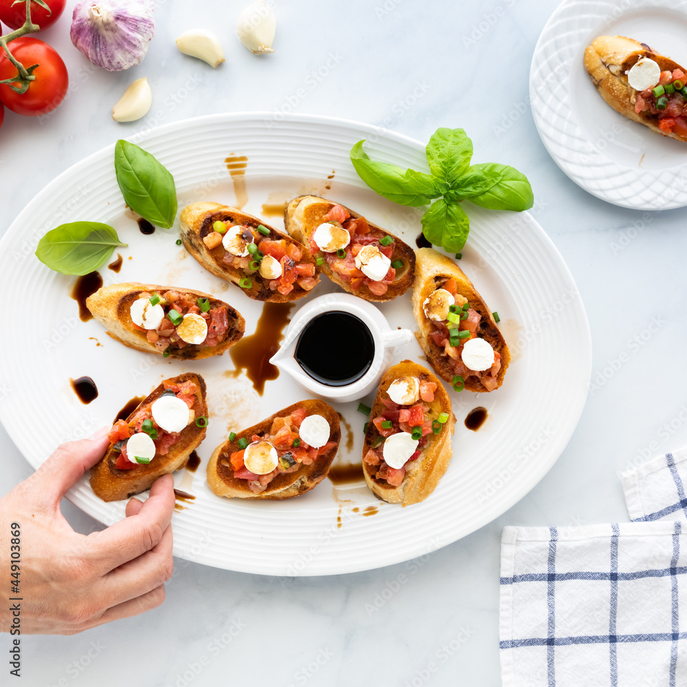 Top down view of a platter of bruschetta with a hand taking one from the platter. Top down view of a platter of bruschetta with a hand taking one from the platter.