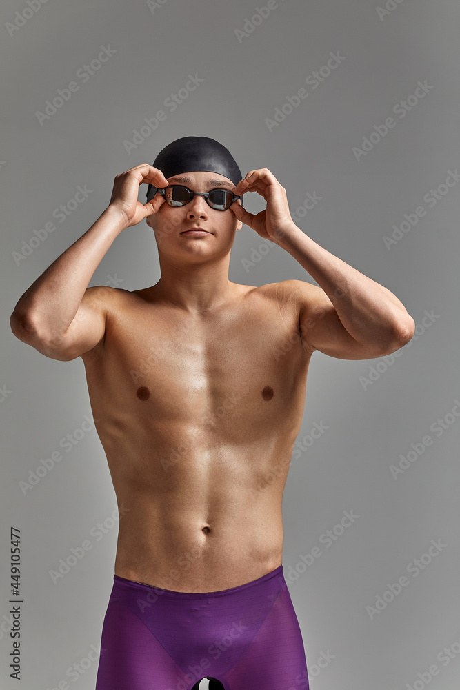 Young male swimmer preparing for the start, close-up portrait of a swimmer in a mask and a hat, gray background, copy space, swimming concept.
