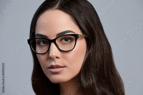 Portrait of a beautiful brunette woman in glasses close-up, attractive woman in stylish glasses on a gray background with healthy beautiful color skin, gray background, copy space