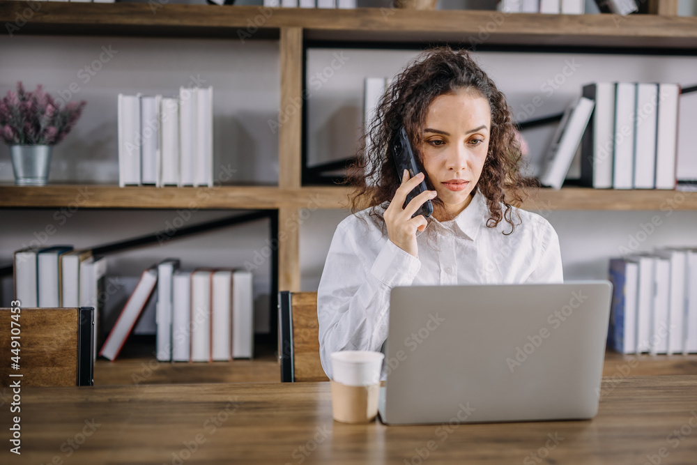 A businesswoman is stressing on the phone with a customer on her desk with her laptop computer and coffee mug at home, work from home concept. A businesswoman is stressing on the phone with a customer on her desk with her laptop computer and coffee mug at home, work from home concept.