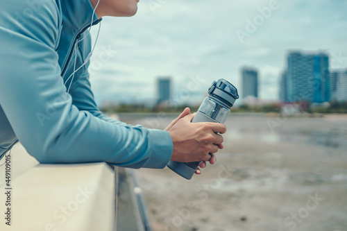 sport man standing after running and holding water bottle drink. Sport thirsty and resting after exercise.
