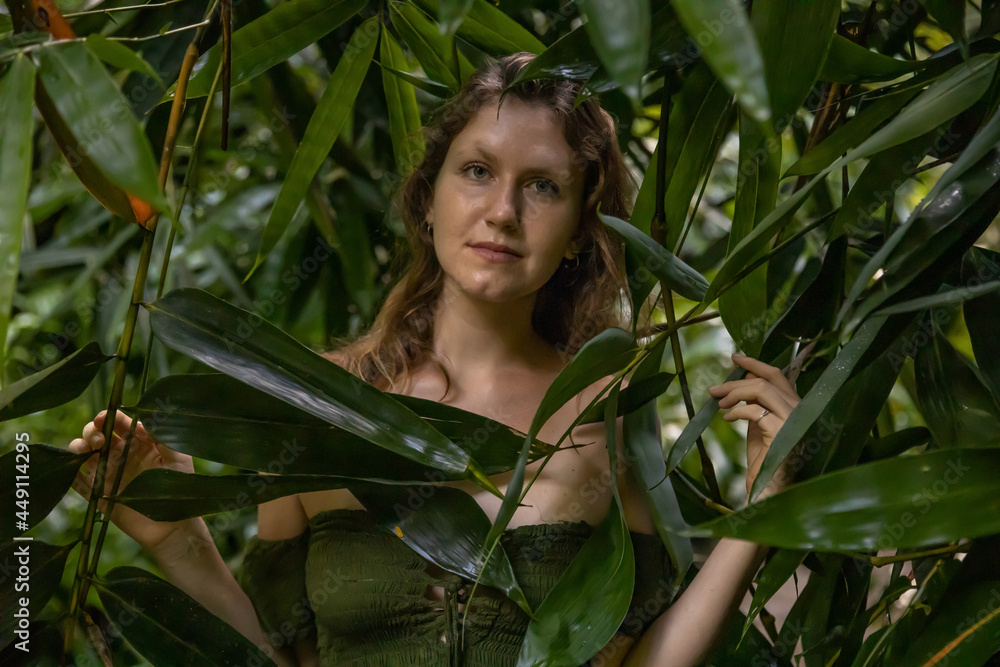 Woman's face surrounded by bamboo leaves. Portrait of beautiful woman in tropical rain forest. Lush green plants in jungle. Nature concept. Bali, Indonesia Woman's face surrounded by bamboo leaves. Portrait of beautiful woman in tropical rain forest. Lush green plants in jungle. Nature concept. Bali, Indonesia
