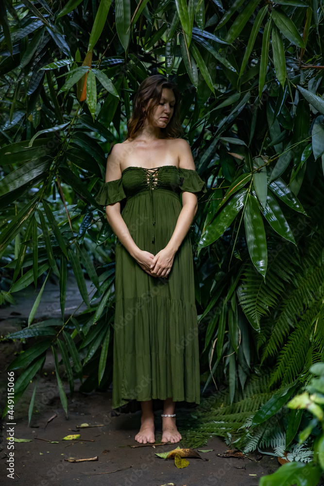 Beautiful woman standing on walking trail in jungle. Caucasian woman wearing long green dress. Bamboo leaves in tropical rain forest. Nature concept. Travel to Asia. Bali, Indonesia