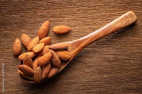 roasted salted almonds in wooden spoon on rustic natural wood texture background, harmony brown tone photo