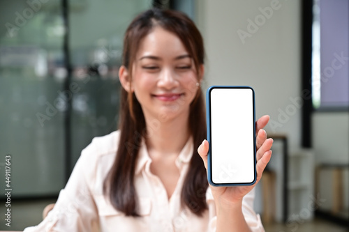 Smiling young woman showing mock up smart phone with blank screen.