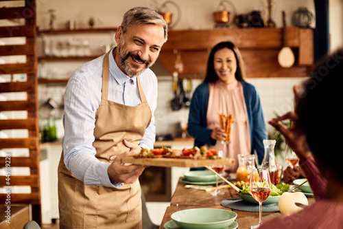 Happy man serves appetizer while having meal with his friends at home.