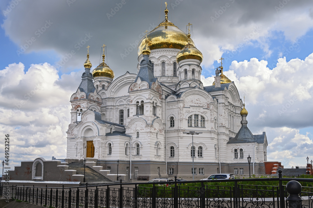 Ancient majestic temple on Belaya Gora (Perm Territory, Russia) on a summer cloudy day. A white-stone temple with golden domes against a textured sky with a large gray cloud before the rain. 