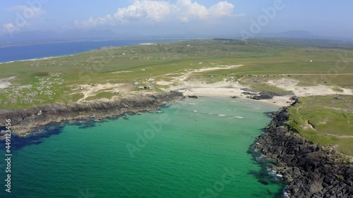 Slyne Head Beach, Clifden, Connemara, County Galway, Ireland, July 2021. Drone faces east, lifts up and pulls away from beach revealing Atlantic coastline with Twelve Ben mountains in the distance. photo