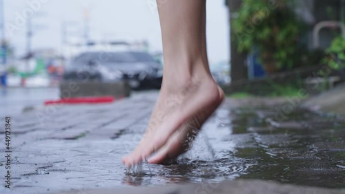 Close up light skin asian girl barefoot stomp and playing on  puddles on the raining day, wet and humid tropical weather in asia, street side area, fun time splashing water, jumping goofy around
