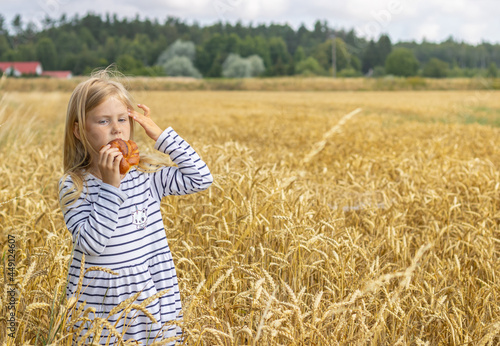 Girl in a striped dress stands in a field and eats a bun