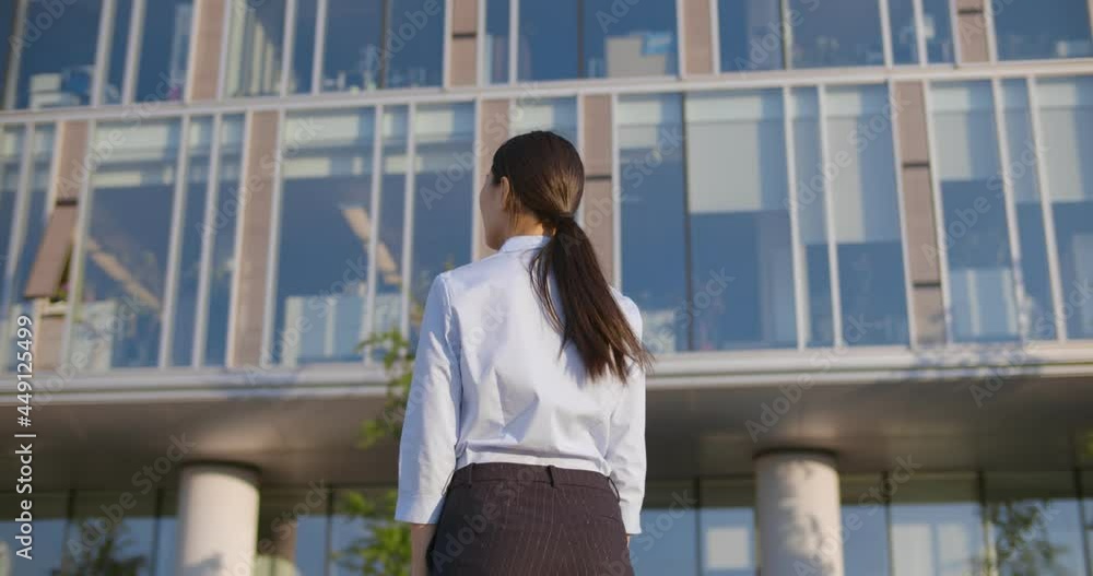 Back view of young businesswoman looking up at modern business center standing outside Back view of young businesswoman looking up at modern business center standing outside