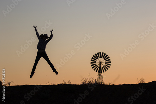 Happy cowgirl jumping and windmill in silhouette photo