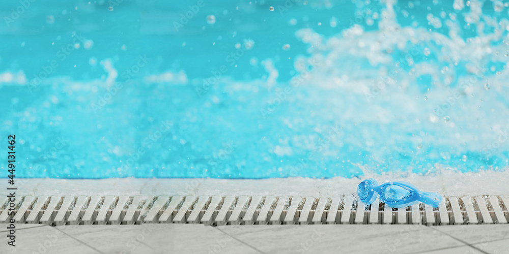 Blue swimming goggles,  at the edge of the pool with water splashes.  Summer vacation concept, swimming training, sports activity.