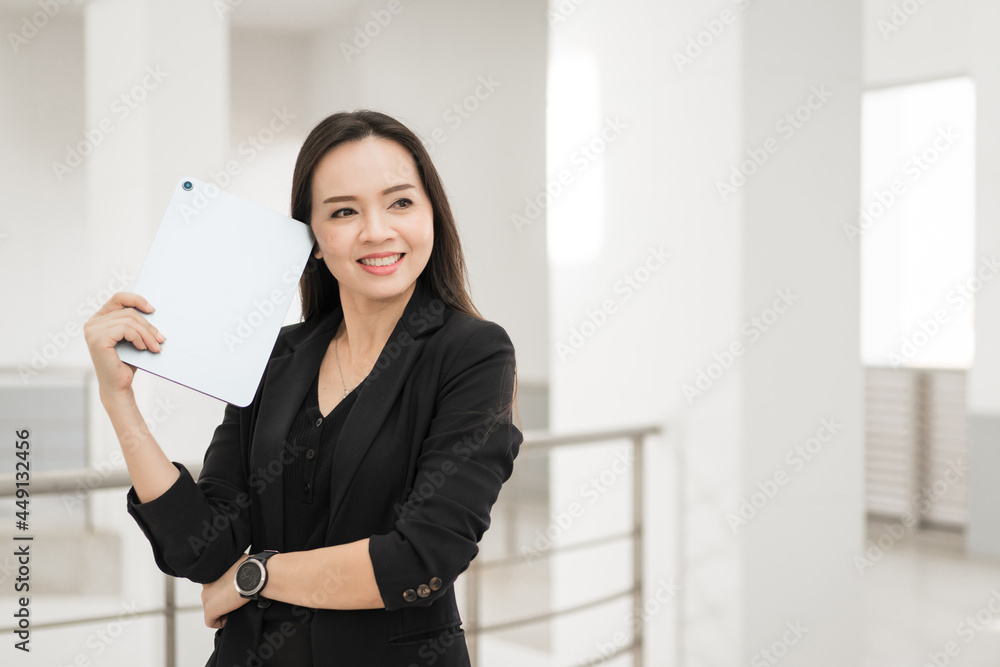 Portrait stock photo of a confident cheerful Asian businesswoman professional in black business suit using a digital tablet standing in the office building representing business oriented concept Portrait stock photo of a confident cheerful Asian businesswoman professional in black business suit using a digital tablet standing in the office building representing business oriented concept