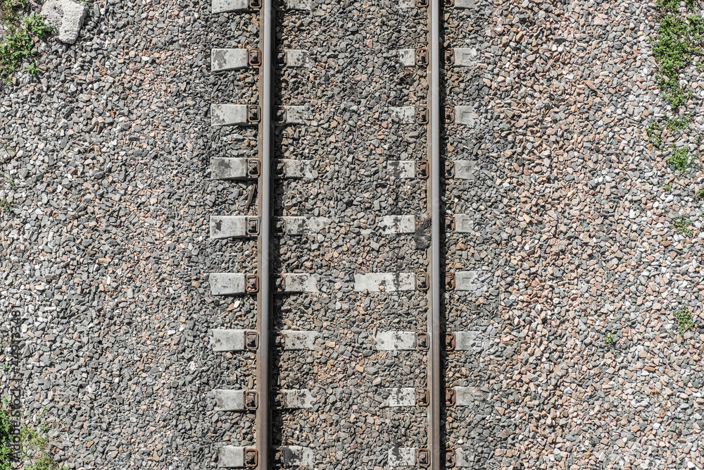 Top view of the railway on a stone track. The texture of the railway and green grass on the sides. Part of the track for trains.