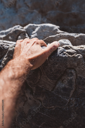 A man with his hand tries to hold on to the mountain by clinging to the ledges in the stone with his fingers