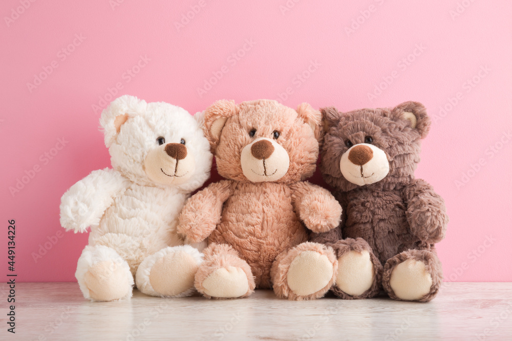 Smiling white, light brown and dark brown teddy bears sitting on table at pink wall background. Pastel color. Togetherness and friendship concept. Front view. Closeup. Smiling white, light brown and dark brown teddy bears sitting on table at pink wall background. Pastel color. Togetherness and friendship concept. Front view. Closeup.