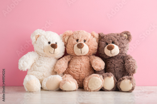 Quadro su tela Smiling white, light brown and dark brown teddy bears sitting on table at pink wall background