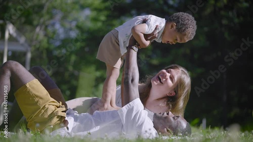 A multicultural family lies in the park. The black father, the half-breed boy and the mother are enjoying a summer day.