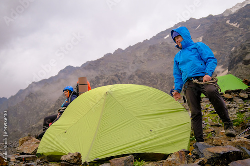 Happy tourist stands at the green tent. Climbing Kazbek from the north, from the side of Russia.