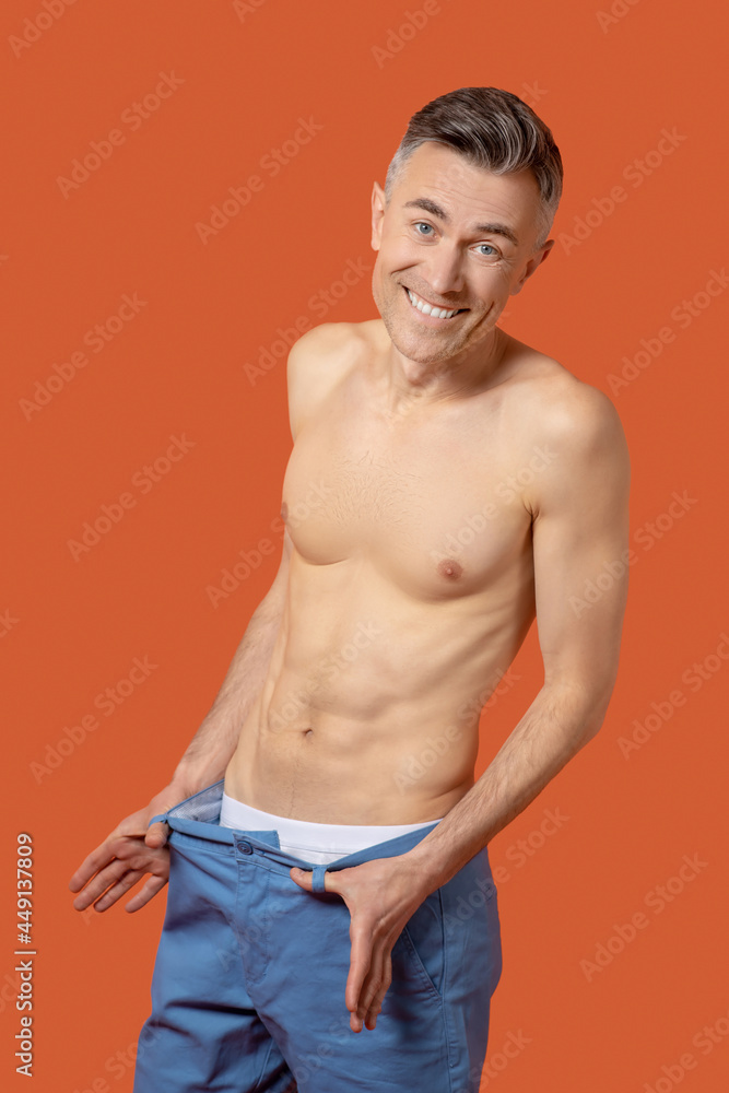 Cheerful man topless in plus size trousers
